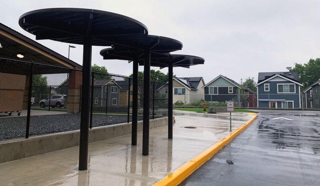 a canopy made of three circles on metal poles is above a sidewalk with a yellow painted curb